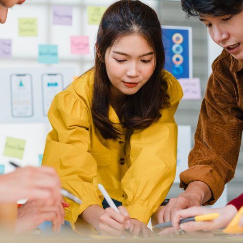 Asian businessmen and businesswomen meeting brainstorming ideas about creative web design planning application and developing template layout for mobile phone project working together in small office.